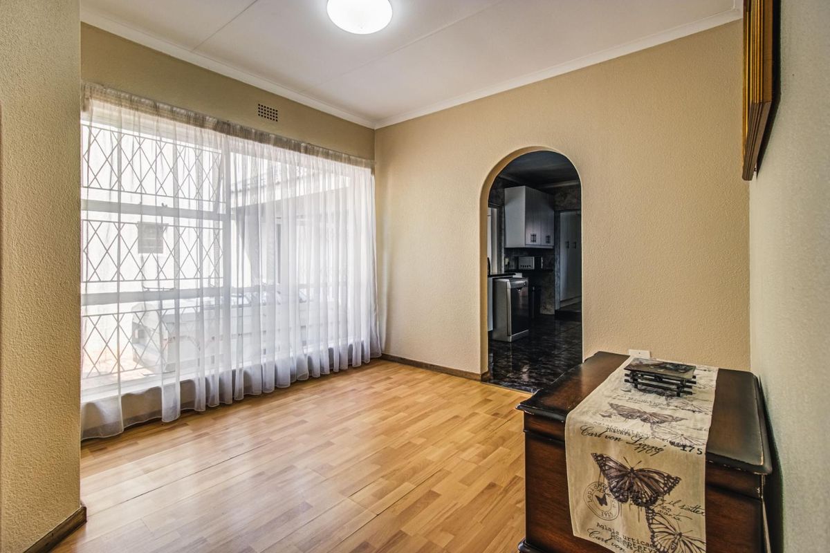 A bright, empty living room featuring laminate flooring, an arched doorway leading to the kitchen, and a large window with security bars.