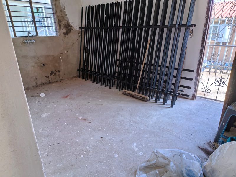 An unfinished utility space featuring exposed concrete flooring, wall-mounted plumbing fixtures, and a steel window frame, currently in need of renovation and finishing.