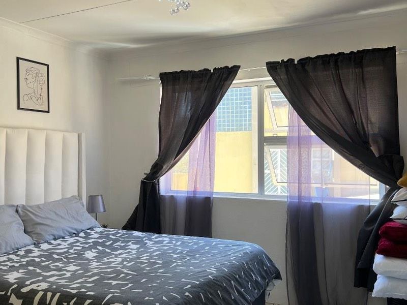 A bedroom featuring tiled flooring, a large window with natural light, and a central ceiling light fixture.