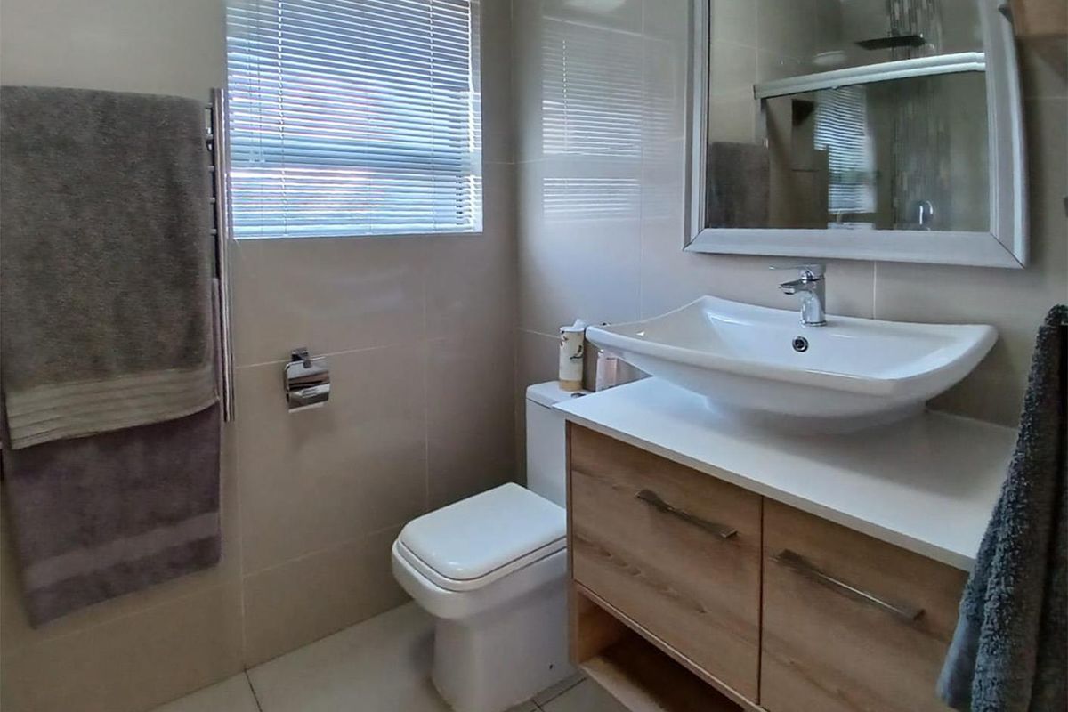 Modern bathroom featuring a contemporary vessel sink vanity, wall-mounted toilet, heated towel rail, and neutral floor-to-ceiling tiling.