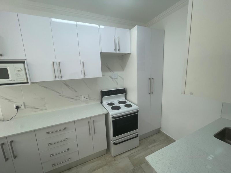 Modern kitchen featuring white cabinetry, stone countertops, marble-look splashback, and a built-in electric stove with integrated microwave.