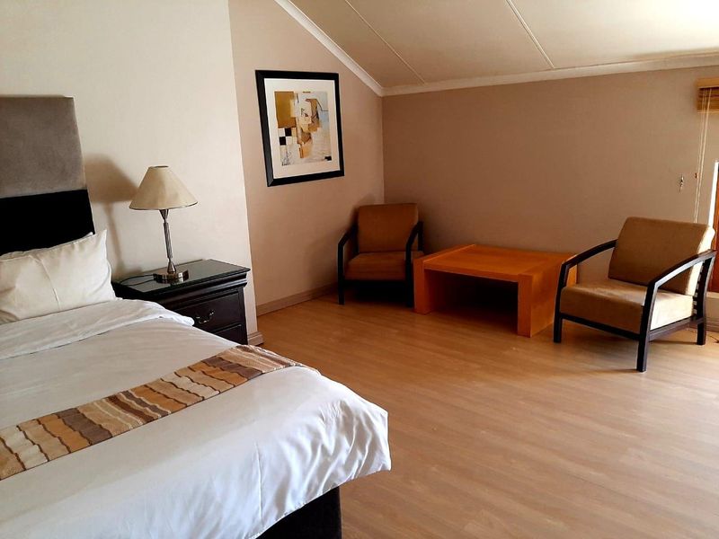 A spacious bedroom featuring light-toned laminate flooring and a distinctive sloped ceiling with cove cornice detailing.