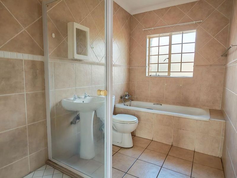 A functional bathroom featuring a pedestal basin, a built-in bathtub, and a separate shower enclosure with tiled finishes throughout.