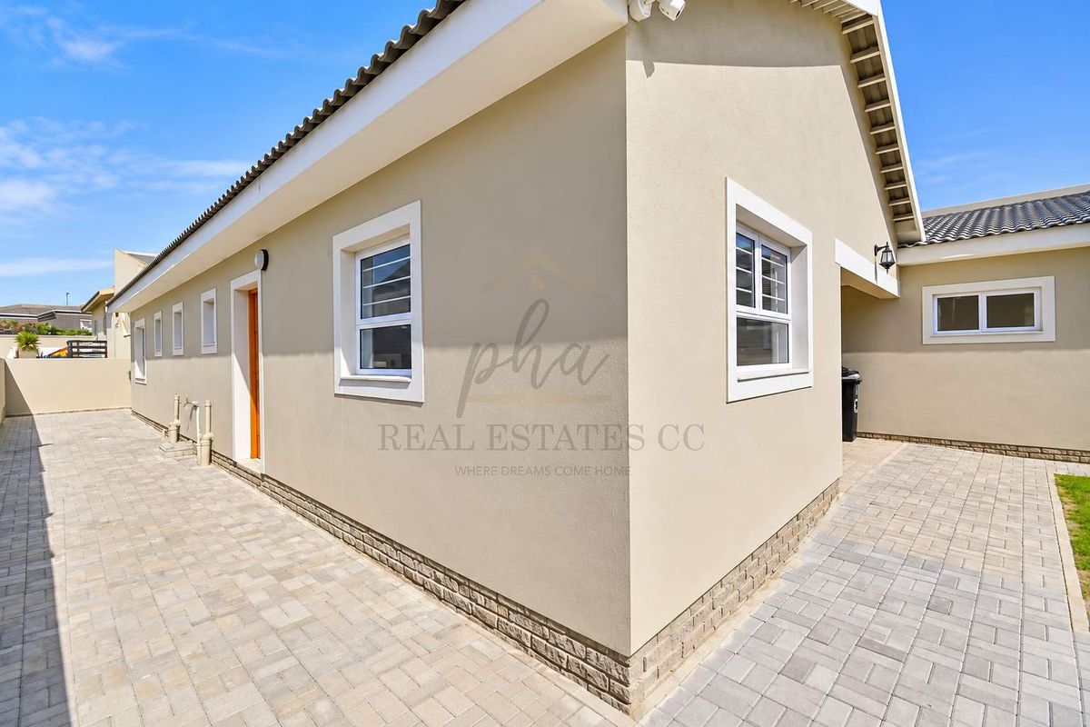 A well-maintained rear exterior view of the property featuring paved walkways, clean rendered walls, and secure window fixtures.