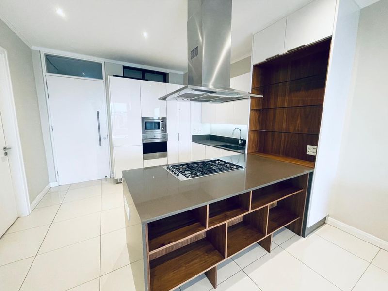 Modern kitchen featuring a central island with gas hob, stainless steel extractor, built-in appliances, stone countertops, and high-gloss cabinetry with integrated shelving.