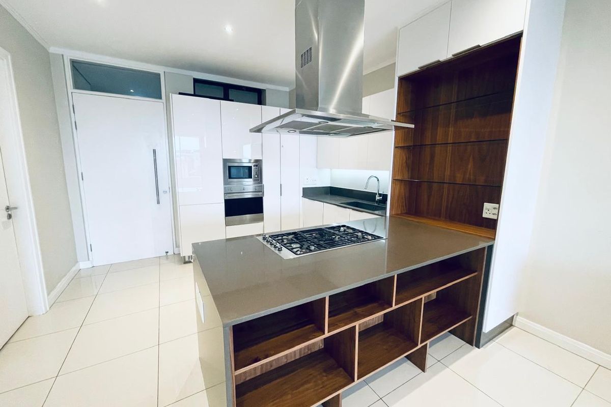 Modern kitchen featuring a central island with gas hob, stainless steel extractor, built-in appliances, stone countertops, and high-gloss cabinetry with integrated shelving.