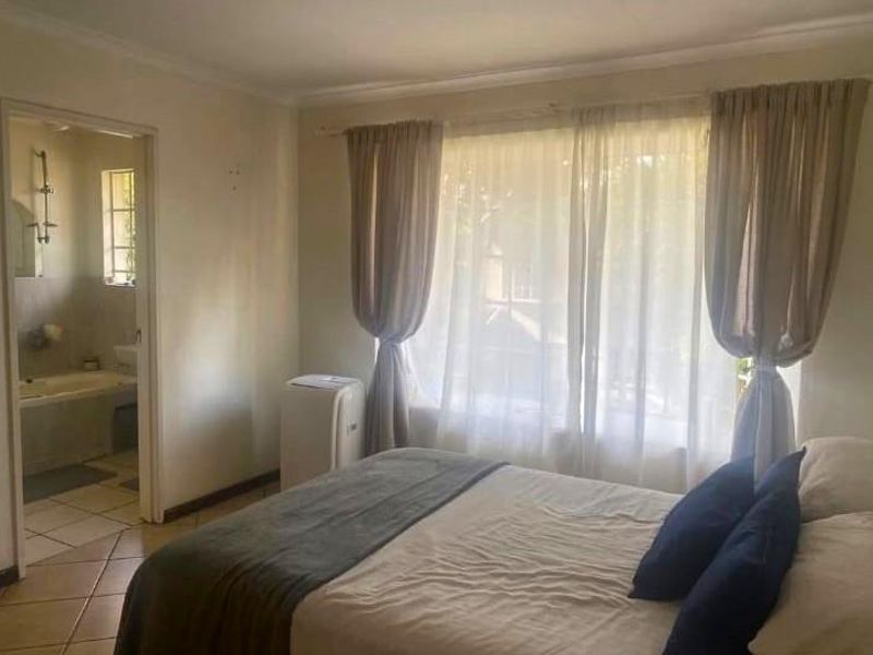A bedroom featuring tiled flooring and an adjoining en-suite bathroom, offering a functional layout with natural light through large windows.
