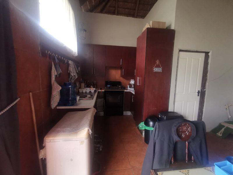 A compact kitchen featuring dark wood cabinetry, a gas stove, and tiled flooring under a traditional thatched ceiling.