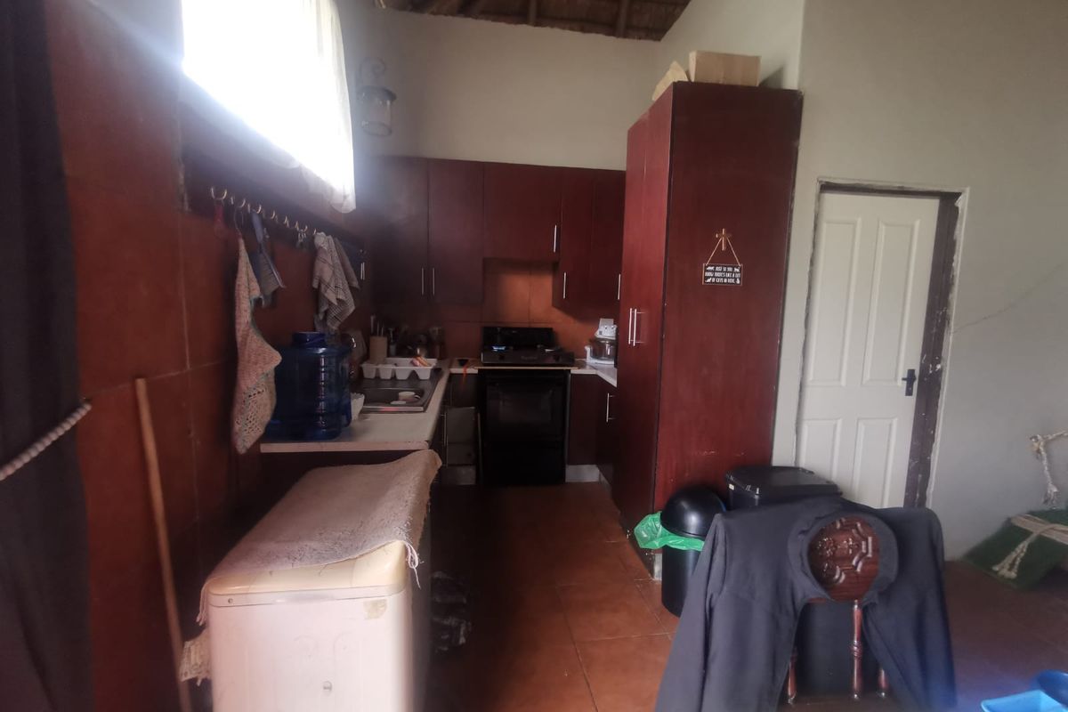 A compact kitchen featuring dark wood cabinetry, a gas stove, and tiled flooring under a traditional thatched ceiling.