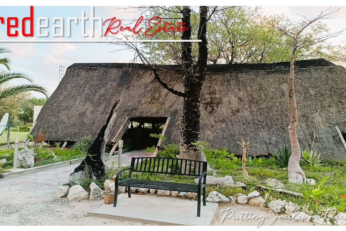 Exterior view of a traditional lodge building featuring a prominent thatched roof, set within a landscaped garden area with paved pathways.