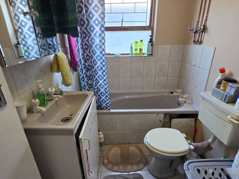 A functional bathroom featuring a bathtub, toilet, and pedestal basin, requiring cosmetic updates to modernize the dated finishes and address minor structural wear.