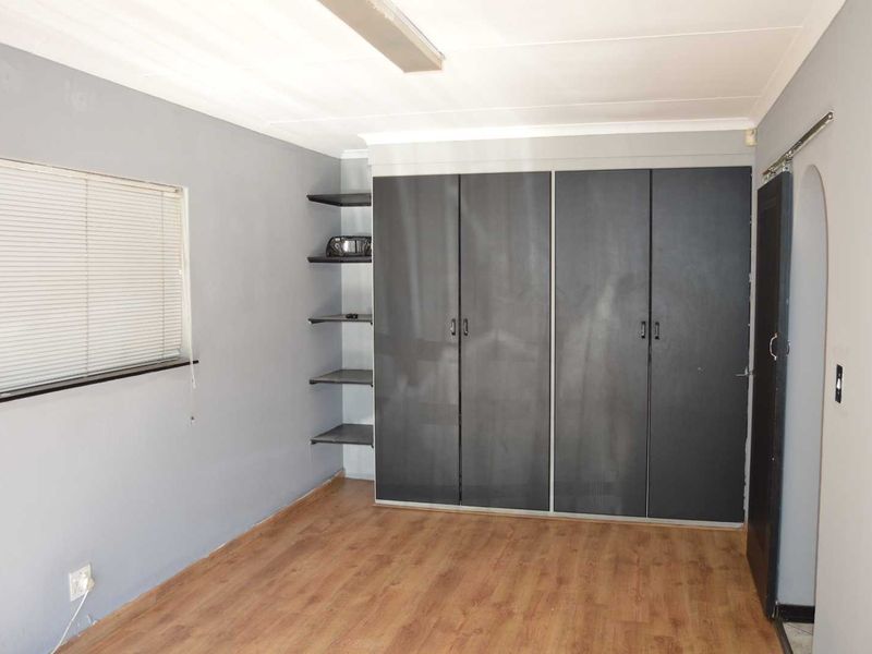 A vacant bedroom featuring laminate flooring, built-in cupboards with open shelving, and venetian blinds.