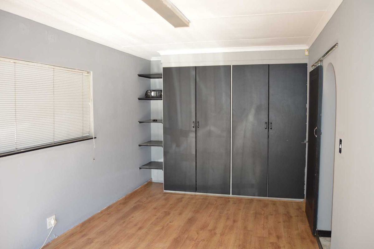 A vacant bedroom featuring laminate flooring, built-in cupboards with open shelving, and venetian blinds.