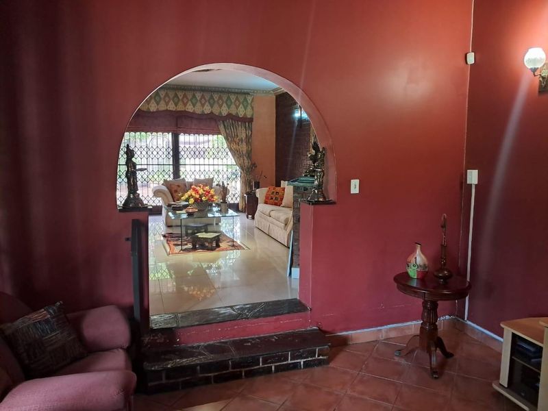 A living room featuring a distinctive arched doorway leading to an adjacent lounge area with tiled flooring and security gate access.