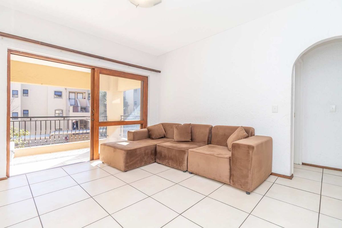 Bright living room featuring white tiled flooring, an arched entryway, and a large sliding glass door providing access to the balcony.