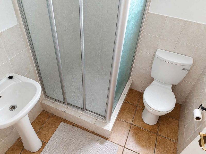 A functional bathroom featuring a shower enclosure, pedestal basin, and toilet with neutral wall and floor tiling.