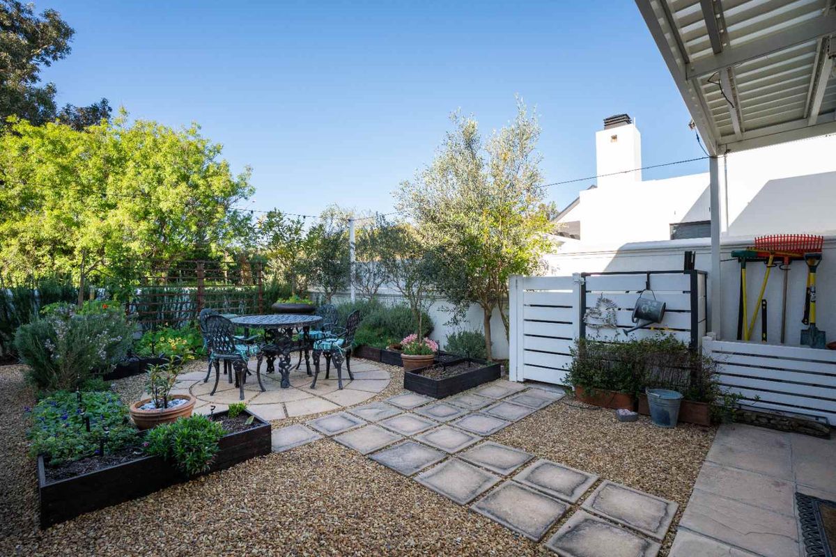 A well-maintained rear garden featuring a paved patio area, raised garden beds, gravel landscaping, and a covered outdoor space.