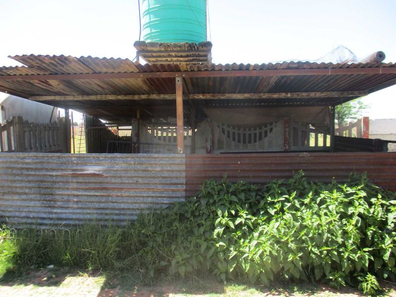 An outdoor utility structure featuring a corrugated iron roof and a mounted water storage tank, set within a fenced agricultural area.