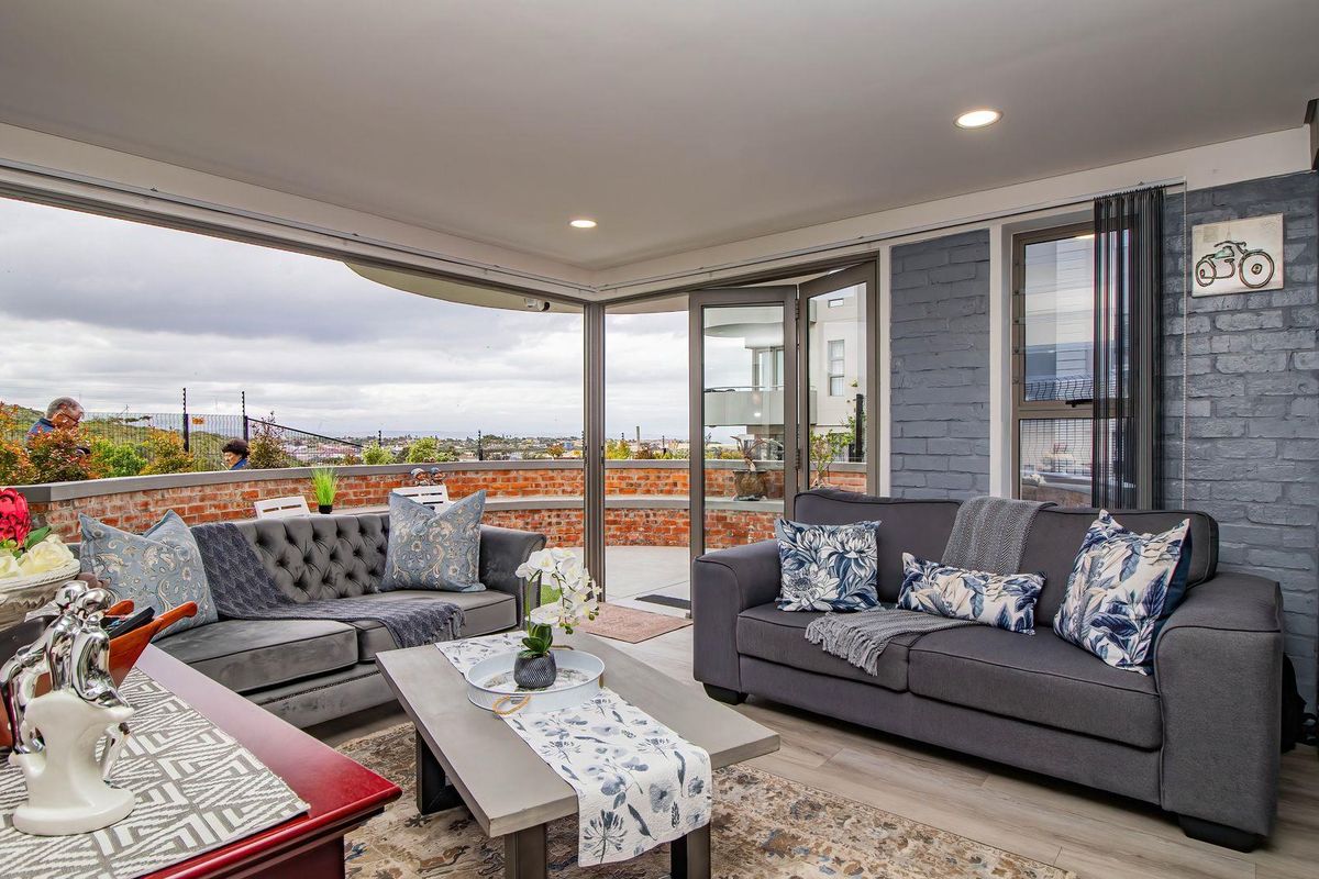 A bright living room featuring modern laminate flooring, a painted brick feature wall, and large bi-fold doors opening onto an outdoor balcony area.