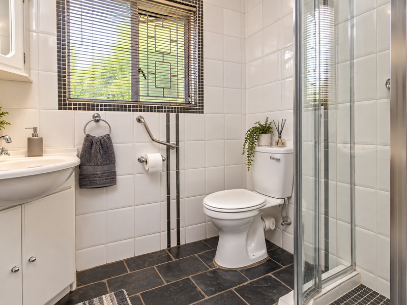A functional bathroom featuring a vanity unit, toilet with grab rail, and a glass-enclosed shower with tiled finishes.