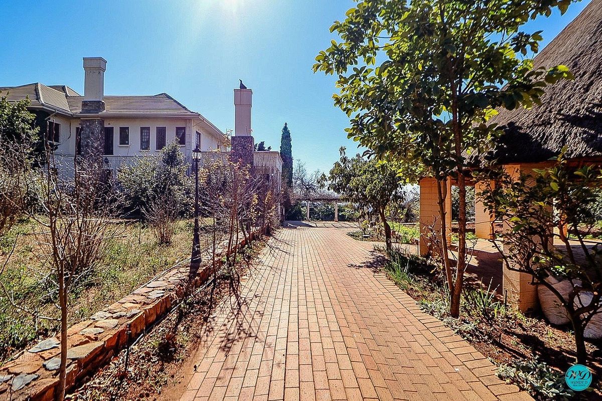 A scenic view of the rear garden featuring a brick paved pathway, stone retaining wall, and a charming thatched roof outdoor structure.
