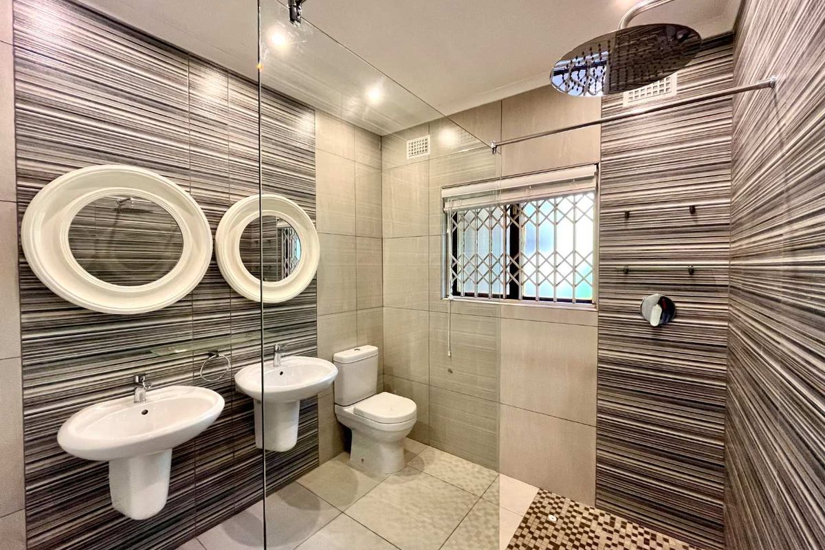 Modern bathroom featuring a walk-in shower with rain shower head, double pedestal sinks, and contemporary tiled finishes.