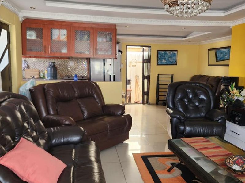 Open plan living area featuring tiled flooring, decorative crown molding, and a kitchen space with wooden cabinetry and a tiled backsplash.
