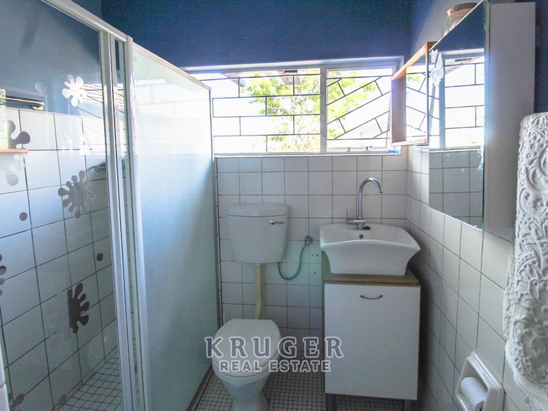 A functional bathroom featuring a shower enclosure, toilet, and vanity basin with tiled walls and natural light from a window with security bars.