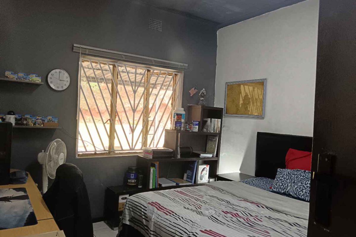 A functional bedroom featuring tiled flooring, a window with security bars, and neutral wall tones, providing a practical space for rest and study.