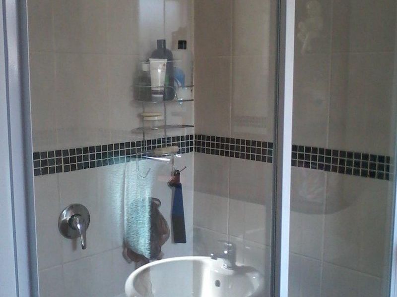 A functional bathroom shower enclosure featuring neutral wall tiles with a decorative mosaic border and a glass sliding door.