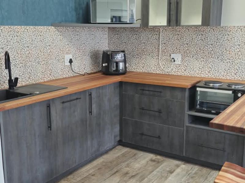 Modern kitchen featuring dark grey cabinetry, warm wooden countertops, a tiled backsplash, and integrated oven and hob, complemented by wood-look laminate flooring.