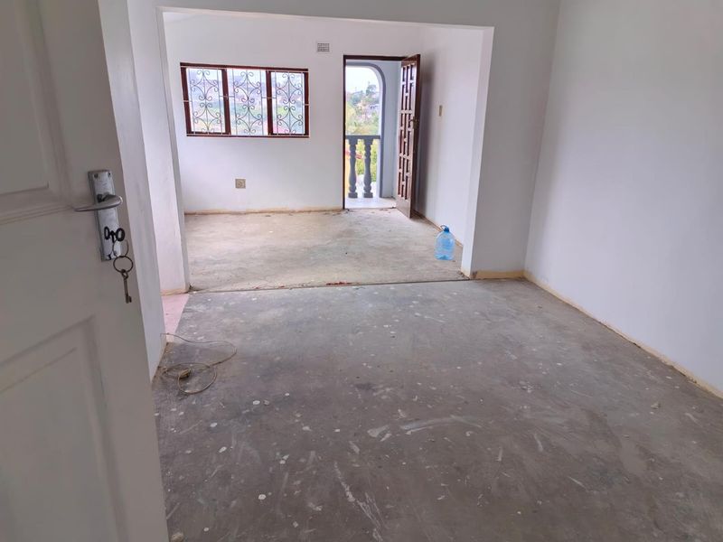 An empty, unfinished living area featuring exposed concrete flooring, security bars on windows, and direct access to an outdoor balcony space.