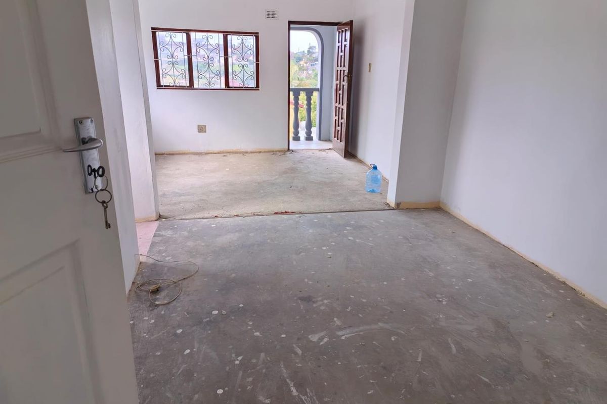 An empty, unfinished living area featuring exposed concrete flooring, security bars on windows, and direct access to an outdoor balcony space.