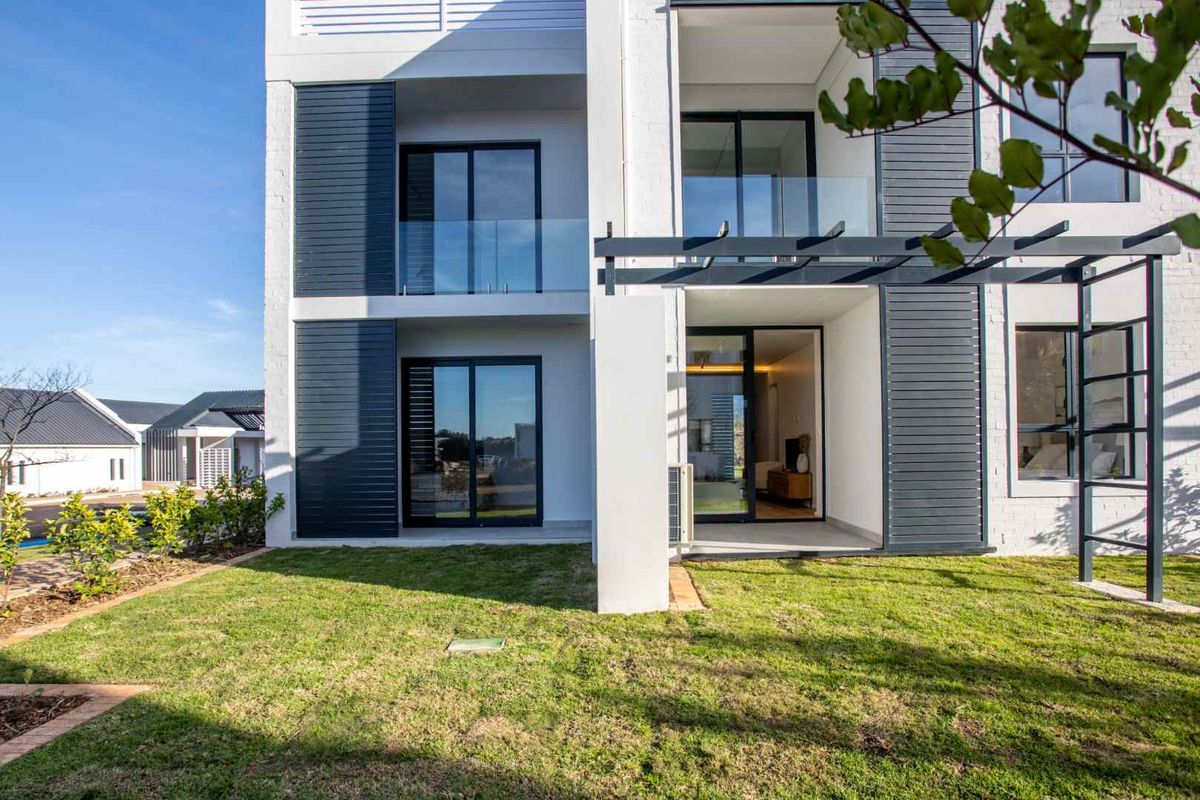Rear elevation of a modern apartment building featuring glass balustrades, sliding doors, and a timber pergola overlooking a private garden area.