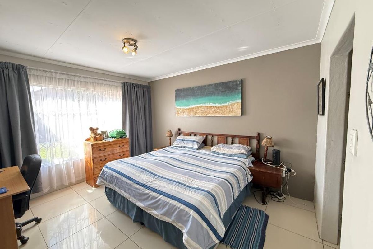 A spacious bedroom featuring large format floor tiles, neutral wall tones, and a large window allowing for natural light.