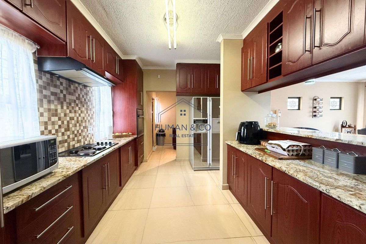 A functional kitchen featuring dark wood cabinetry, granite countertops, a gas hob, and a tiled backsplash, offering ample storage and workspace.