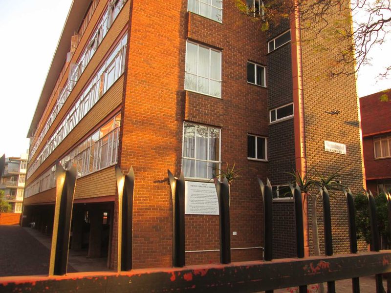 Exterior view of a multi-story brick apartment building featuring steel-framed windows and secure perimeter fencing.
