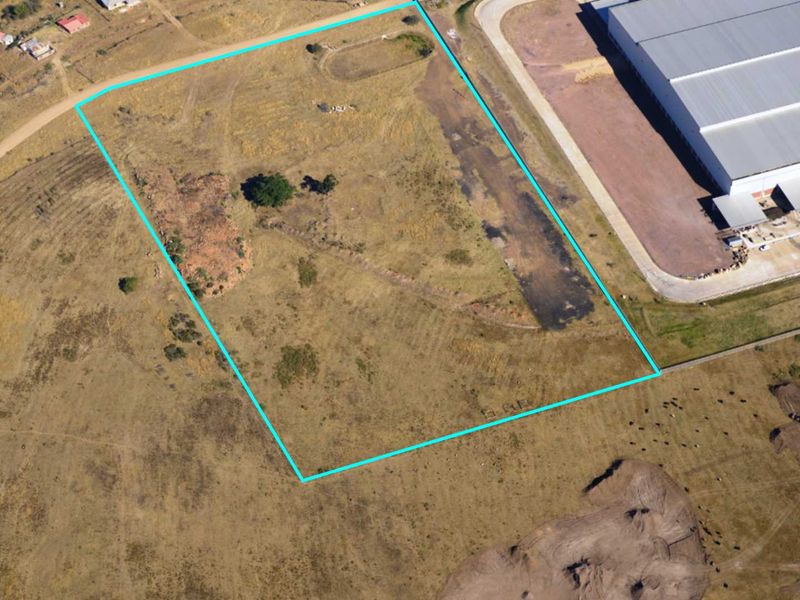 Aerial view of a vacant commercial land plot with clear boundary markings, situated adjacent to existing industrial infrastructure.