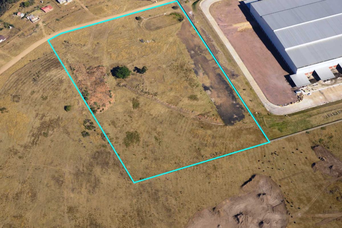 Aerial view of a vacant commercial land plot with clear boundary markings, situated adjacent to existing industrial infrastructure.