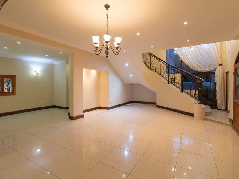 Spacious entrance hall featuring polished tiled flooring, a grand curved staircase with wrought iron balustrade, and elegant lighting fixtures.