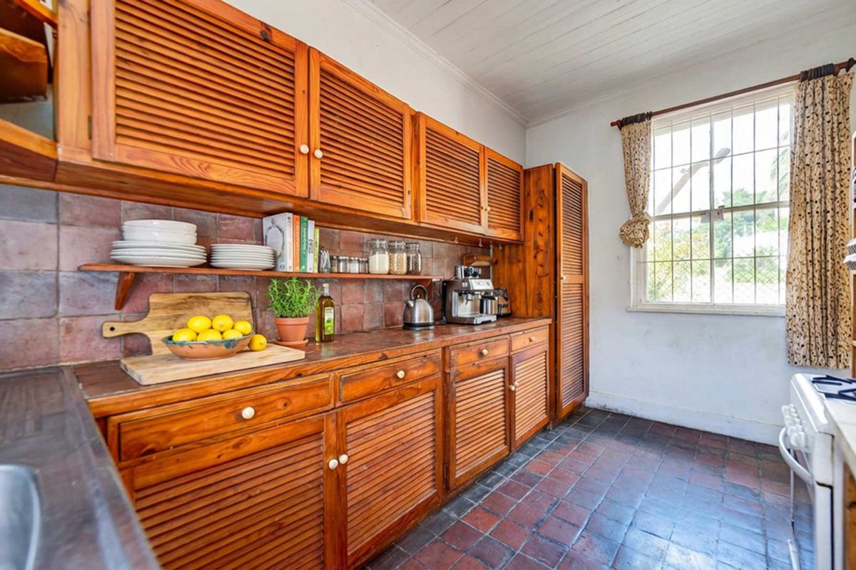 A rustic kitchen featuring traditional wooden louvered cabinetry, terracotta floor tiles, and a tiled backsplash, offering a classic, dated aesthetic.