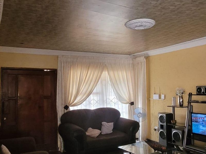 A living room featuring a textured ceiling with a decorative rose, coving, and a security gate on the entrance door.