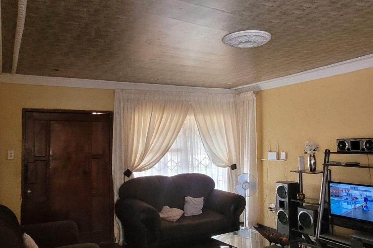 A living room featuring a textured ceiling with a decorative rose, coving, and a security gate on the entrance door.
