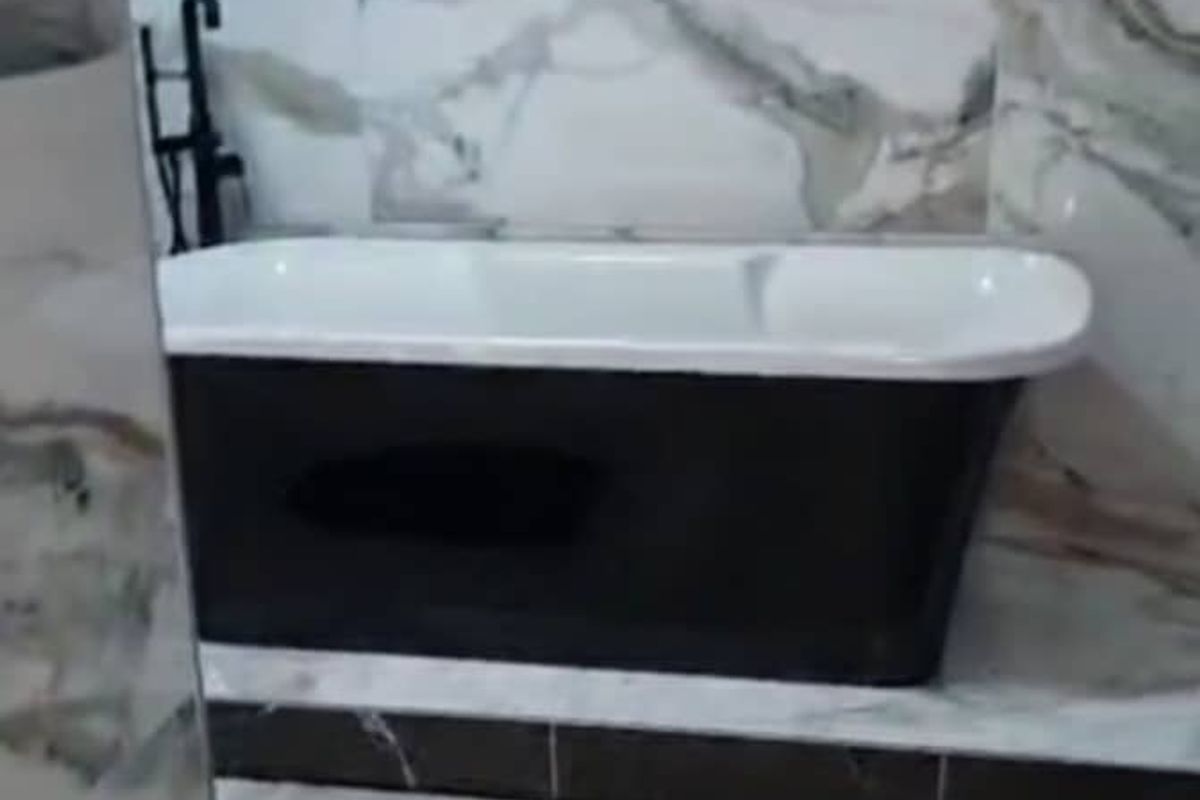 A modern bathroom featuring a sleek black freestanding bathtub set against elegant marble-look wall tiles and wood-effect flooring.