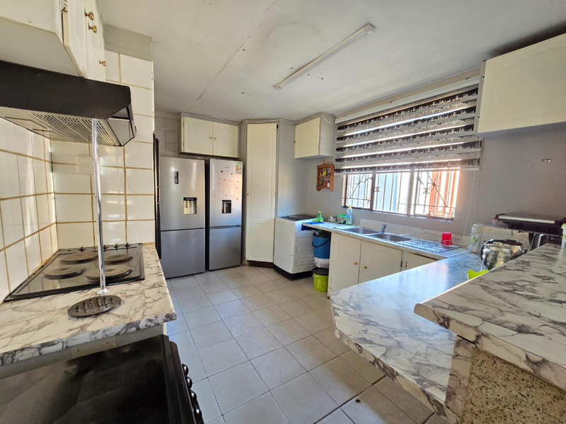 Functional kitchen featuring built-in cabinetry, laminate countertops, electric hob with extractor, and tiled flooring, offering potential for modernization.