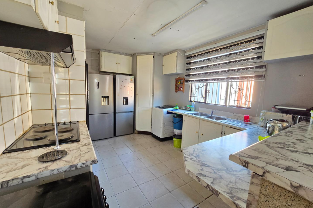 Functional kitchen featuring built-in cabinetry, laminate countertops, electric hob with extractor, and tiled flooring, offering potential for modernization.