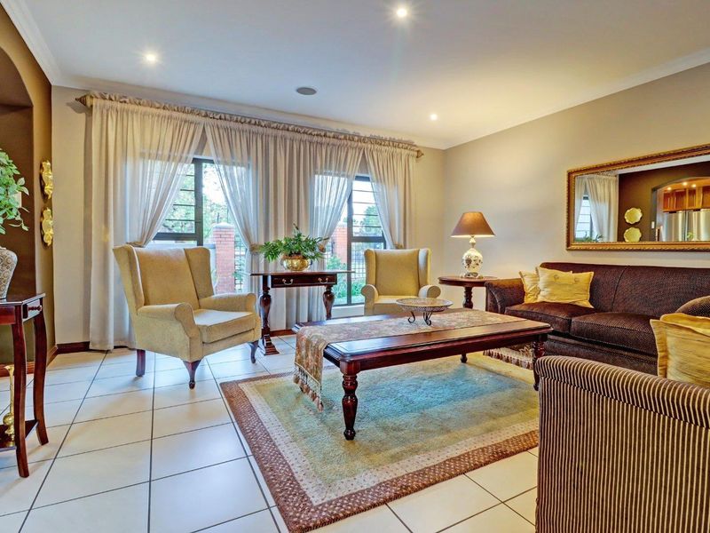 A well-maintained living room featuring neutral tiled flooring, recessed downlighting, and large windows with security bars, offering a bright and comfortable living space.
