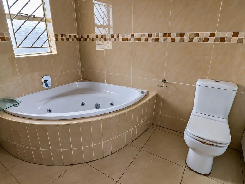 A bathroom featuring a corner spa bath, tiled walls and flooring, and a toilet. The space is functional but would benefit from cosmetic updates.
