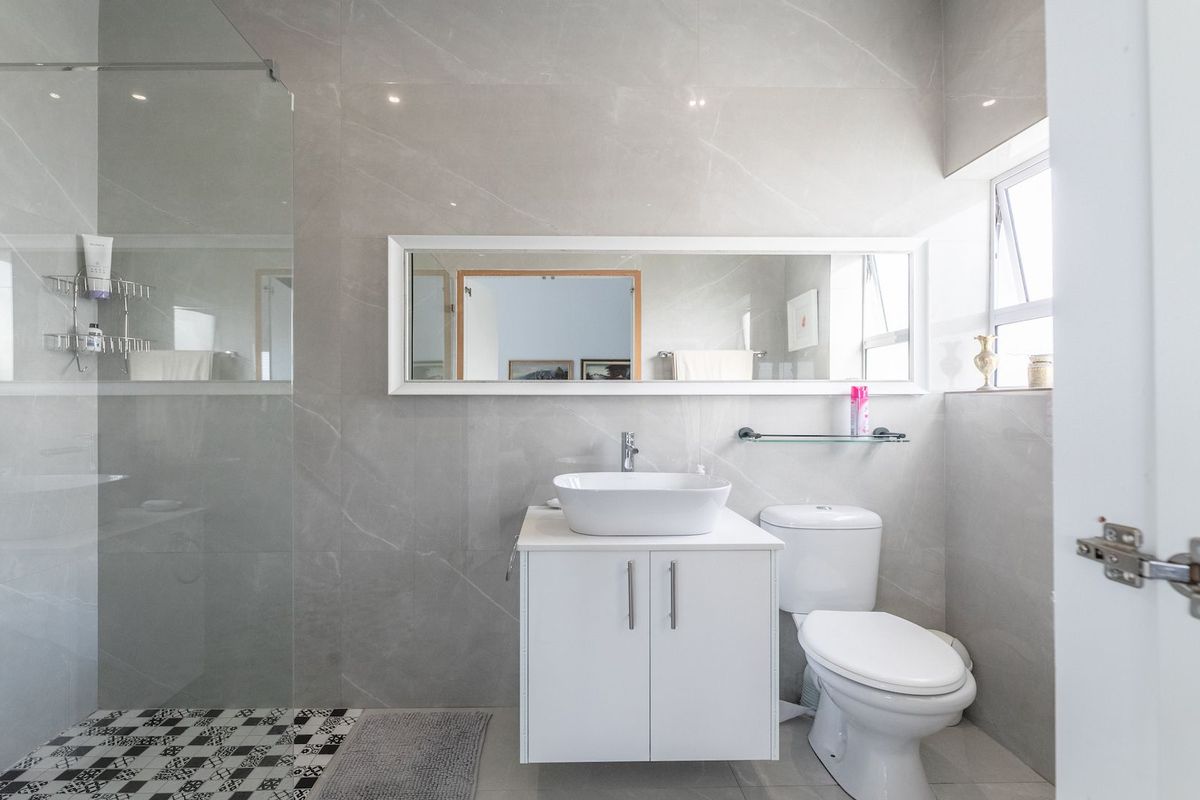 Modern bathroom featuring large format grey wall tiles, a frameless glass shower enclosure, a white vanity with a vessel sink, and a wall-mounted mirror.