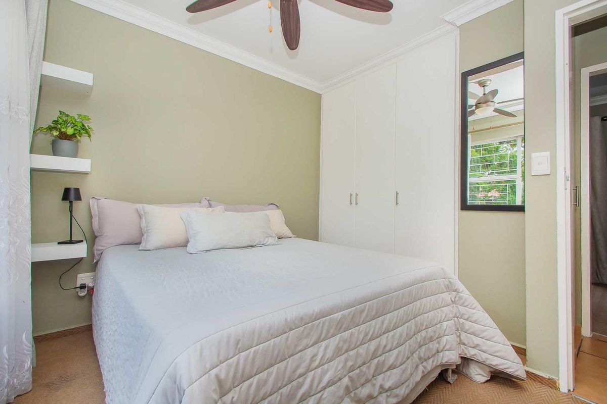 A cozy bedroom featuring built-in white cabinetry, a ceiling fan, and floating wall shelves, finished with neutral wall tones.